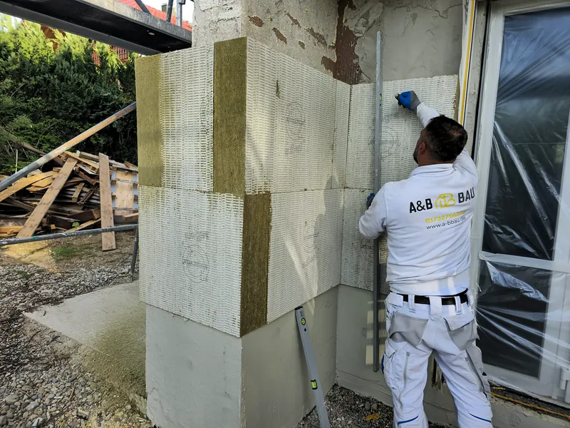 Ein Handwerker von A&B Bau prüft mit der Wasserwaage die Mineralwolle-Dämmplatten an einer Hausecke