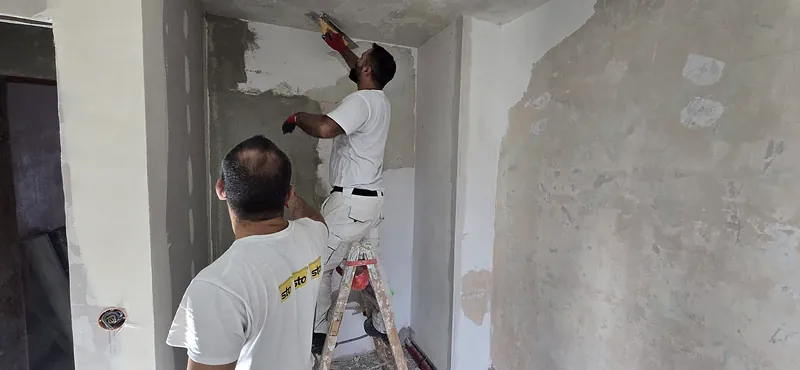Zwei Handwerker von A&B Bau verputzen gemeinsam eine Wand
